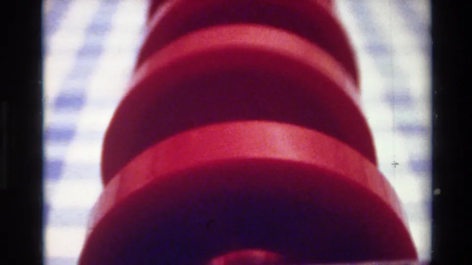 Close 8mm view from the 1980 Big Sur clip, showing a red cylindrical form, likely dumbbell-like, against a pale checkered surface.