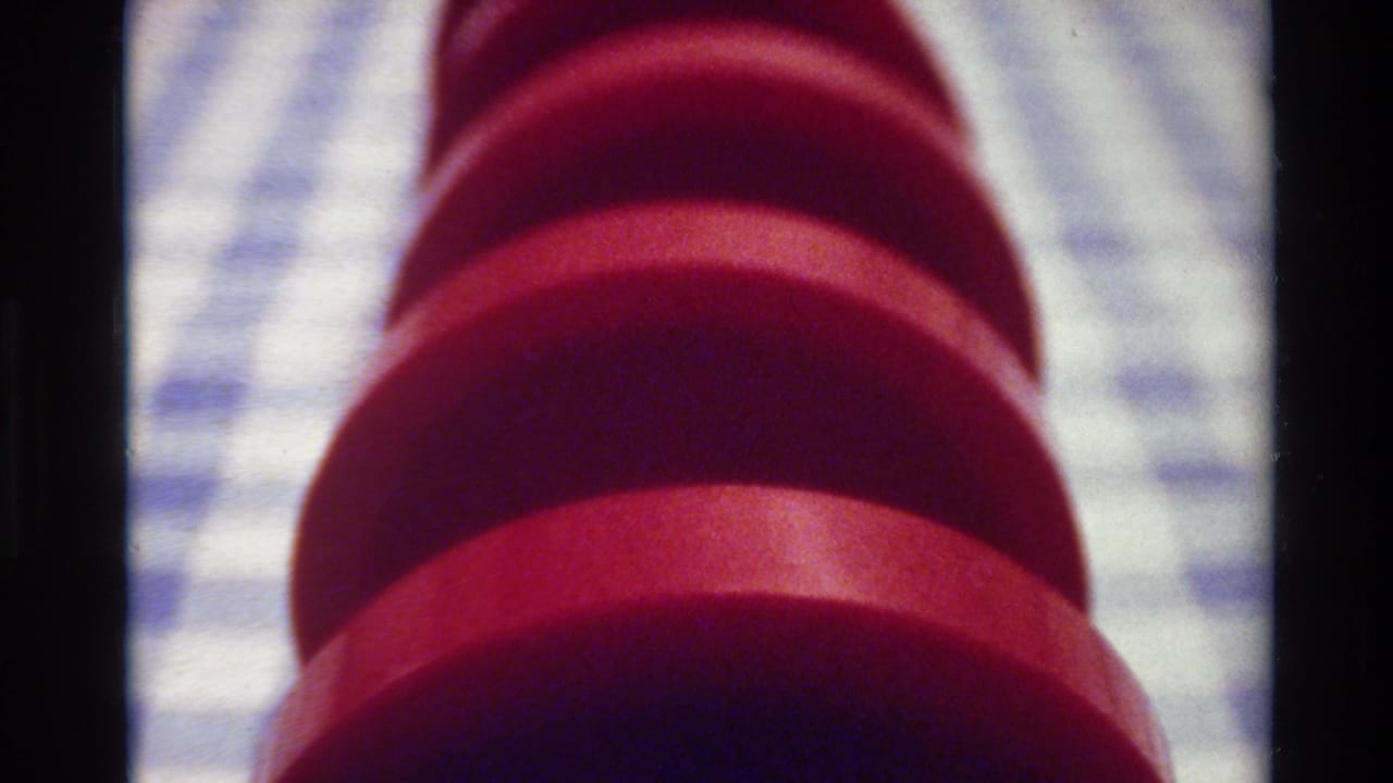 Close view of a red ribbed spiral object on a blue-and-white checkered surface.