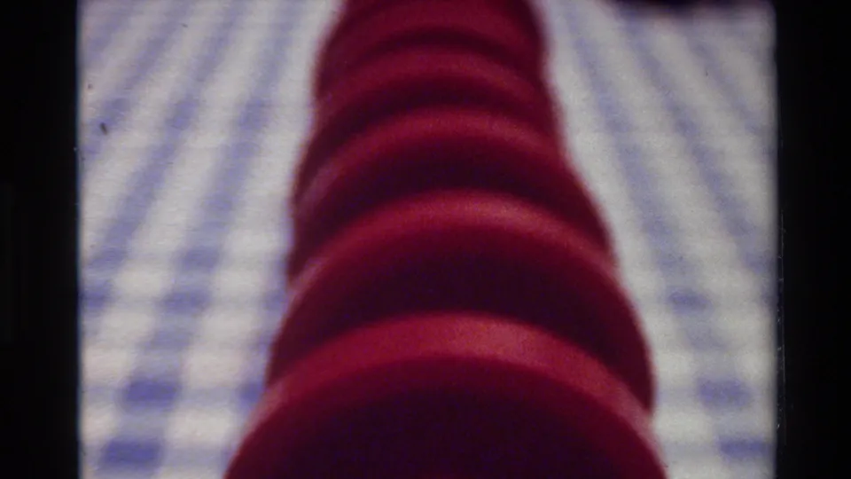 1980 Big Sur 8mm frame with a slightly wider view of the red spiral object on a checkered tabletop surface.