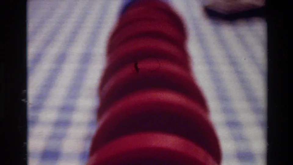 1980 Big Sur 8mm frame showing the red spiral object on checkered cloth, with a dark curved shape near the top edge.