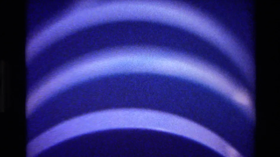 1980 Big Sur home-movie frame showing repeated pale blue curved stripes across a dark blue rounded form.