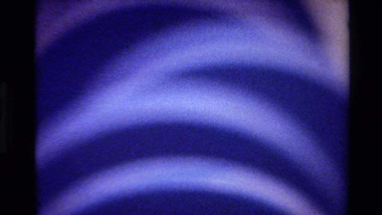 Abstract 1980 Big Sur 8mm frame with blue, fabric-like curved bands, soft highlights, grain, and dark vertical film borders.