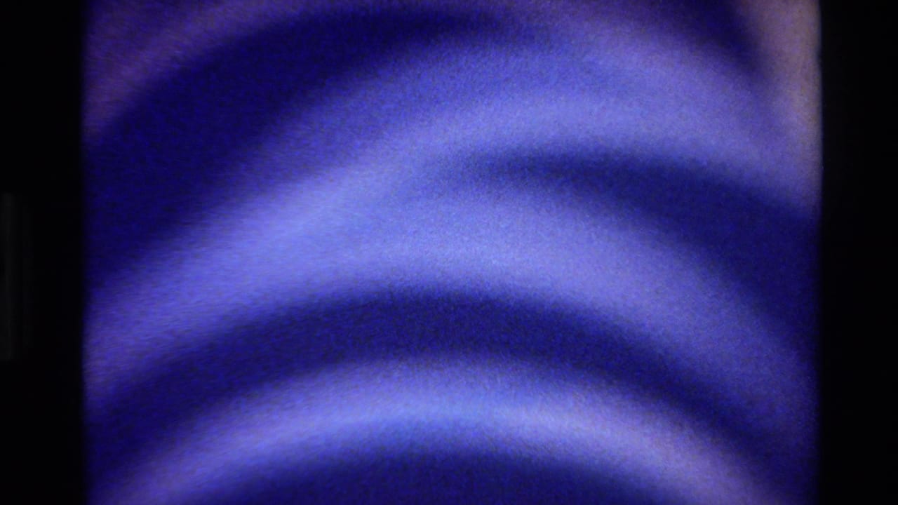 Abstract close-up from the 1980 Big Sur 8mm clip showing blue ripples, pale bands, grain, and a dark film border.