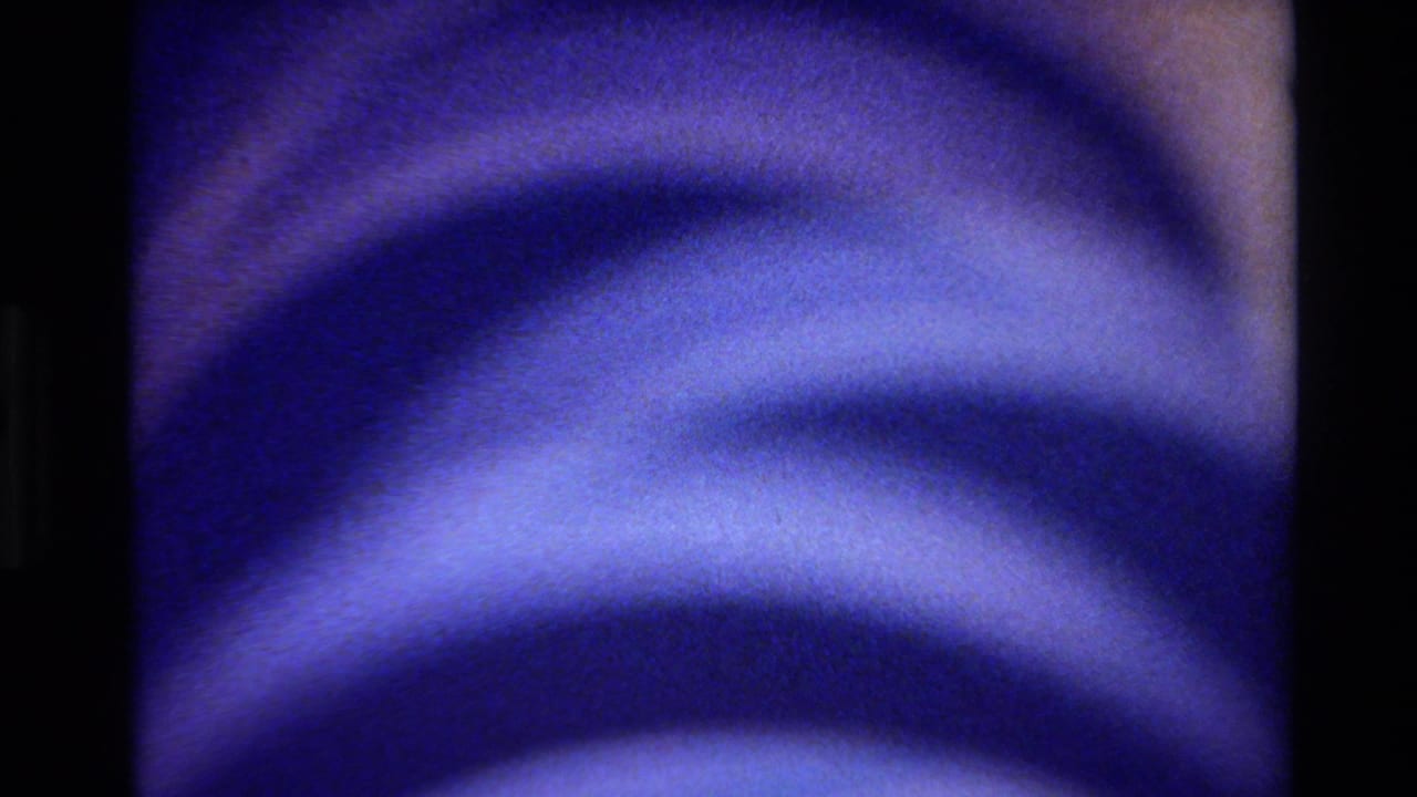 1980 Big Sur 8mm frame showing blue-purple concentric arcs in close-up with soft focus and dark vertical film edges.