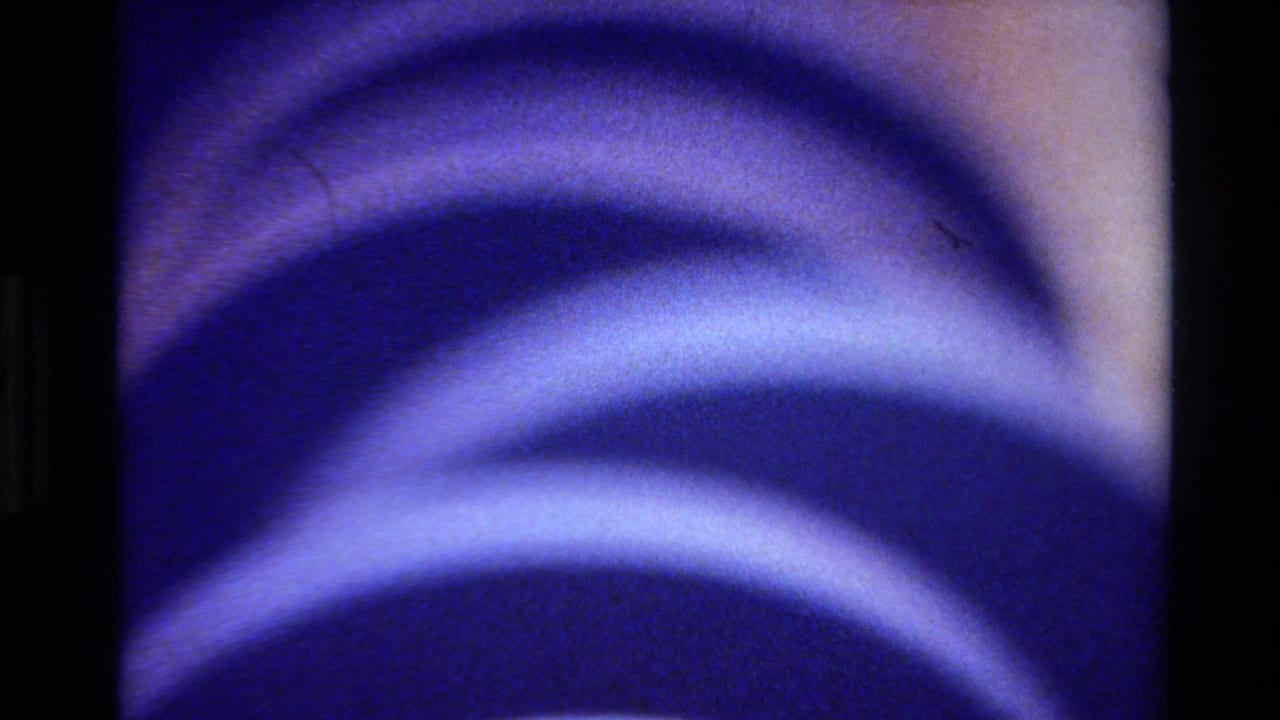 1980 Big Sur 8mm frame with large blue curved bands and purple shadows across a close-up abstract surface.