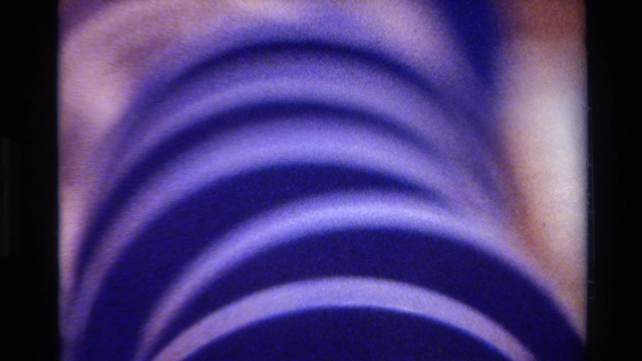 1980 Big Sur 8mm frame showing a close view of a purple segmented hose or tube, with a pale inner part and dark film borders.