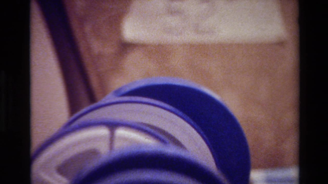 Close view of a handwritten 52 on white tape against a textured surface, with a blue cylindrical object in the foreground from the 1980 Big Sur 8mm reel.