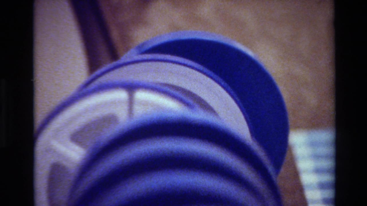 Close-up of a blue 8mm reel in soft focus, with brown storage material and a pale label visible behind it.