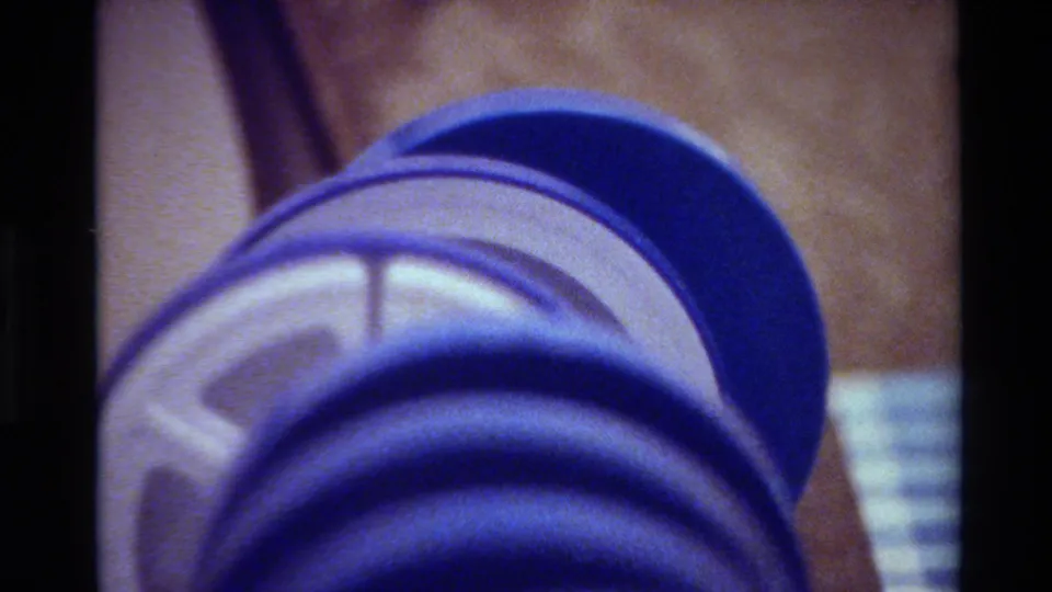 Close-up of a blue 8mm reel in soft focus, with brown storage material and a pale label visible behind it.