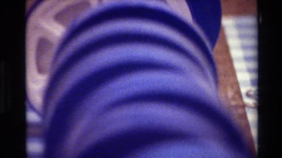 Close 8mm-era view of the blue reel and surrounding wooden surface, with analog blur and color cast.