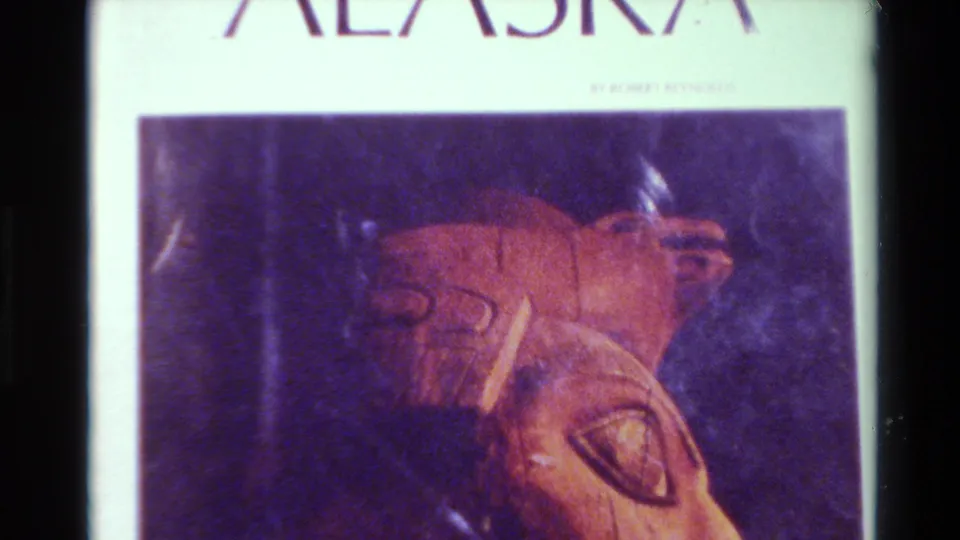 Final 1980 8mm frame showing an ALASKA slide or page with a reddish carved artifact and strong purple-orange film color shift.