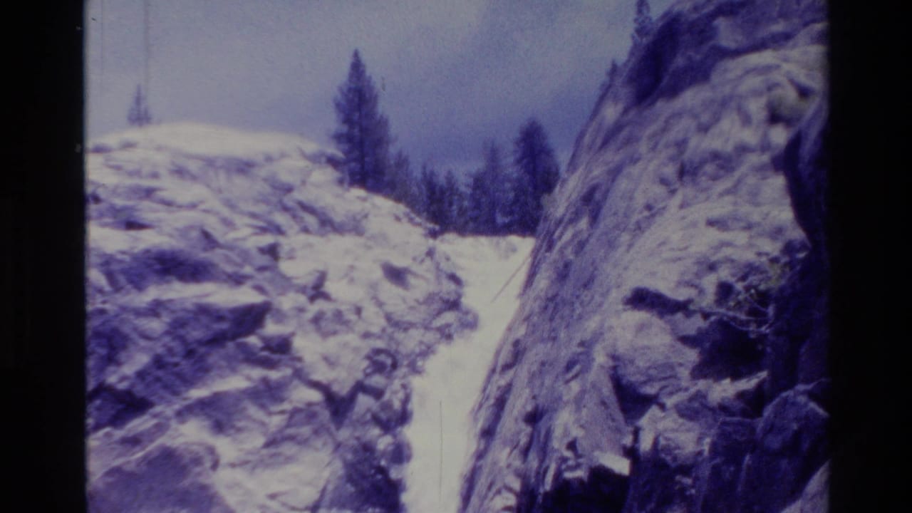 Waterfall descends between rocky canyon walls with trees above.