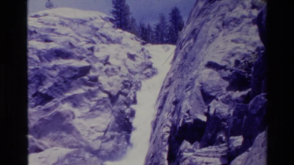 Vintage Big Sur frame showing the waterfall channel and nearby rock face, with snow patches and soft 8mm grain visible.