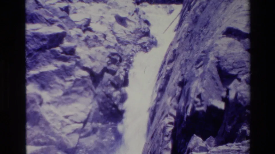 Big Sur home-movie frame with rushing water framed by steep rocks and a strong blue-purple film cast.