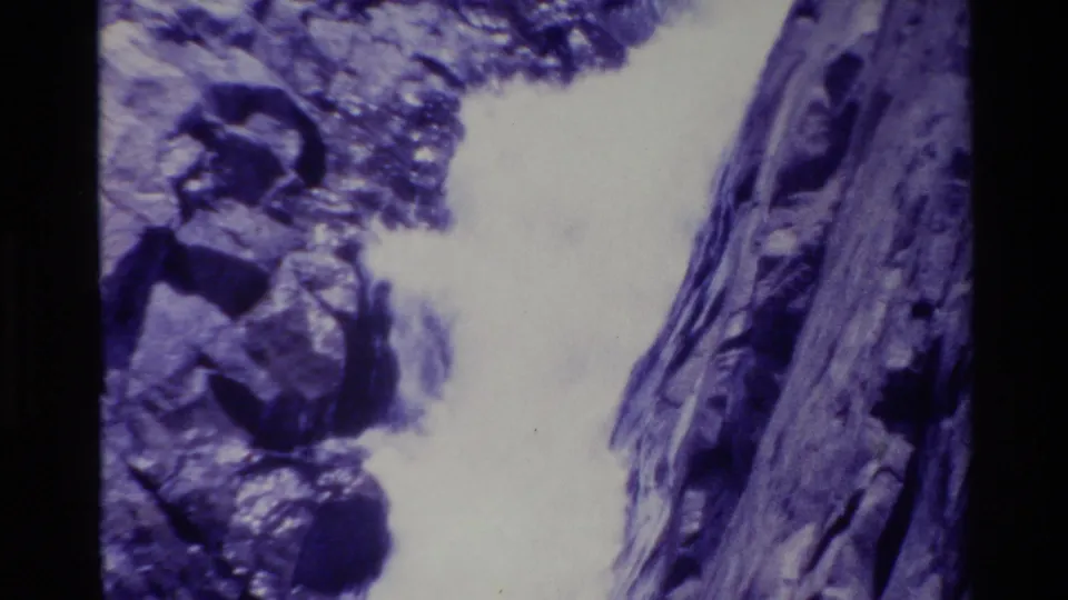 1980 8mm Big Sur frame showing a bright waterfall channel beside jagged shadowed rock faces.