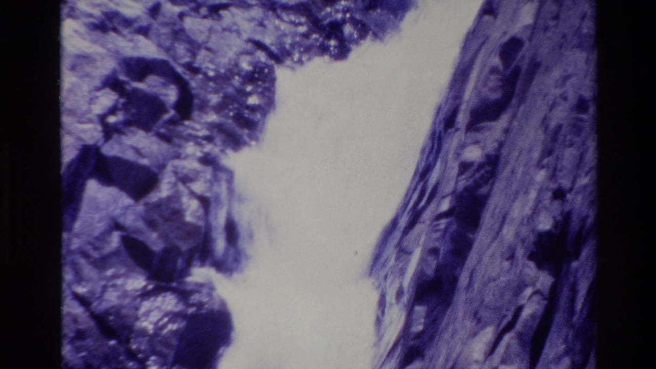 1980 Big Sur 8mm frame showing water cascading between rocks beside a dark vertical natural surface.
