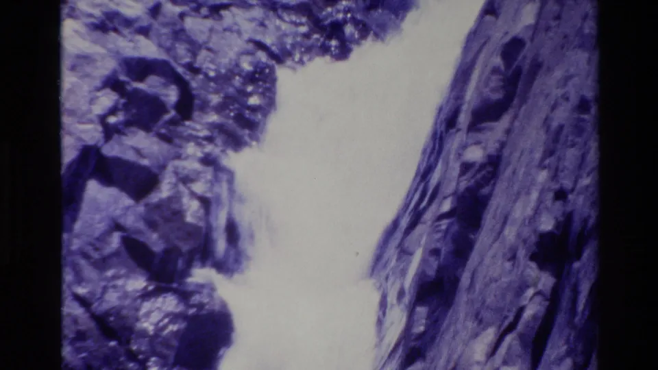 1980 Big Sur 8mm frame showing water cascading between rocks beside a dark vertical natural surface.