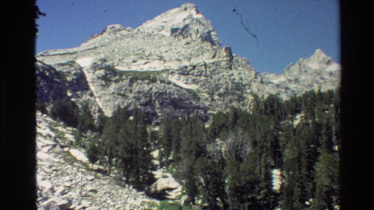 Grand Teton, Wyoming frame from 1980 8mm footage with a rocky mountain wall, conifers, snow, and sky.