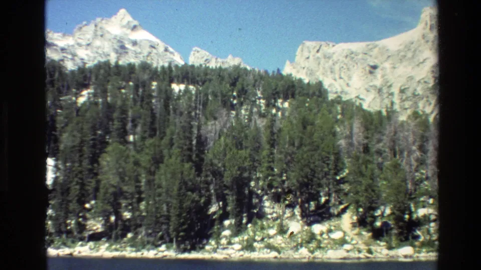 Grand Teton, Wyoming 8mm footage frame showing evergreen forest, rocky terrain, and sunlit snow-capped mountains.