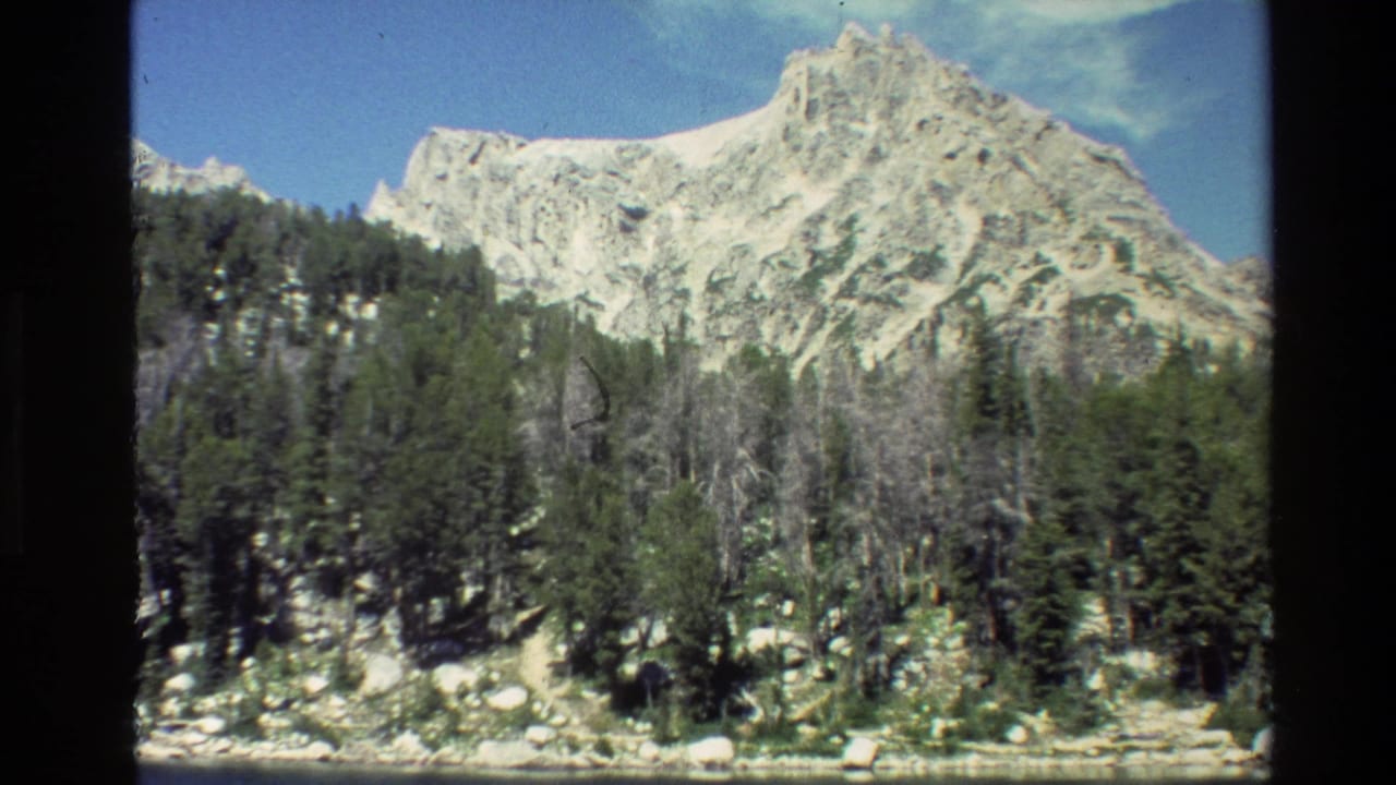 Snow-dusted mountain peak above evergreen forest and a rocky lakeshore.