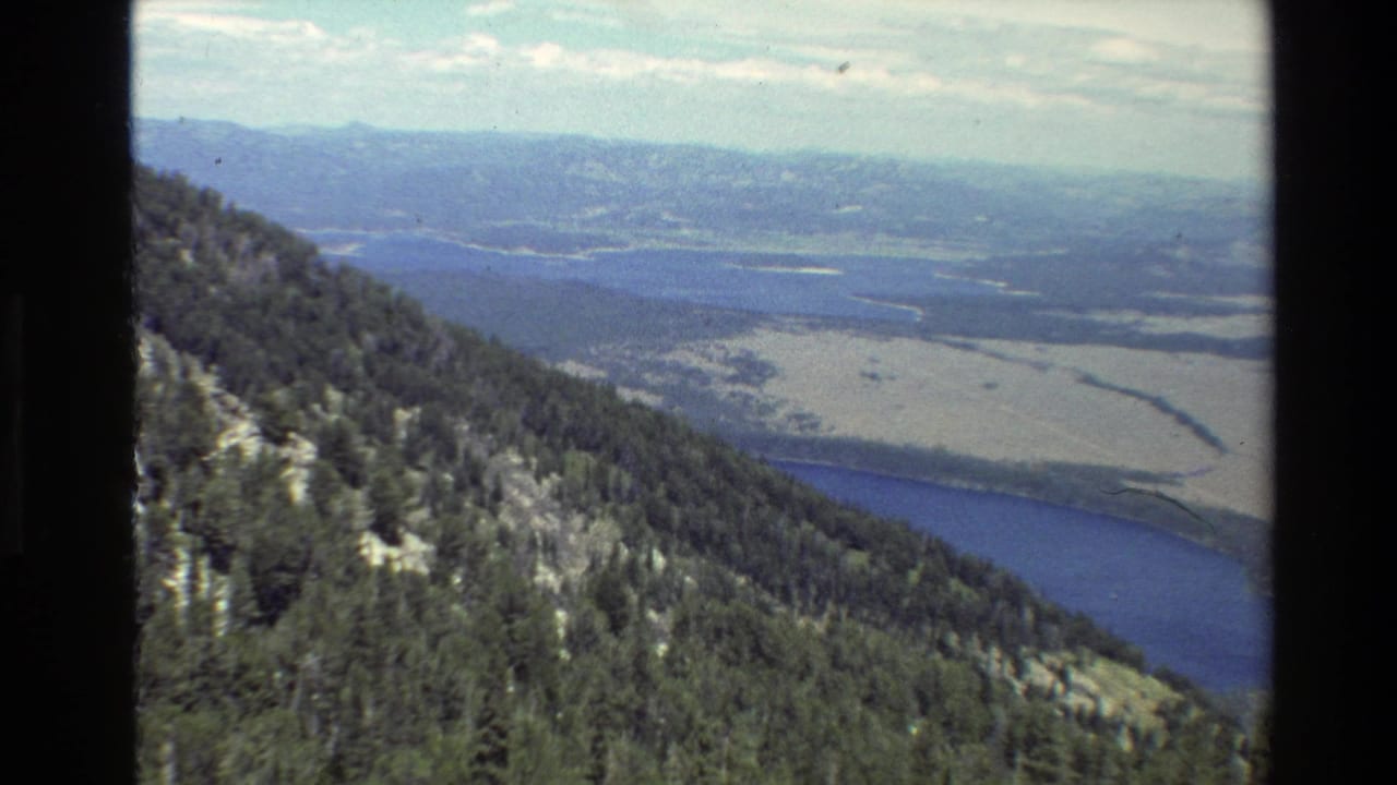 1980 Grand Teton, Wyoming 8mm frame showing conifer-covered slopes above a blue lake, open valley flats and distant ridges.