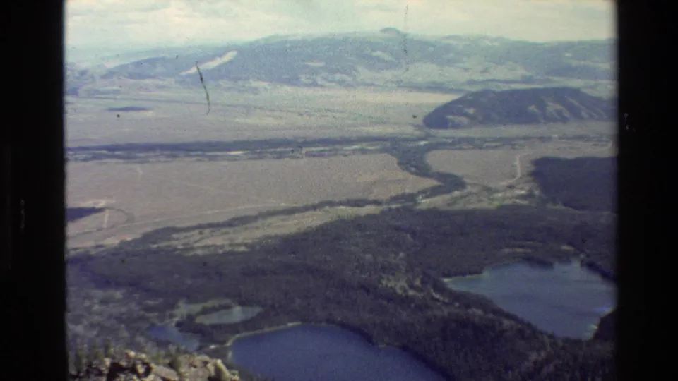 1980 Wyoming home-movie view across forest, small blue lakes, a winding river channel, and hazy hills in the Grand Teton area.