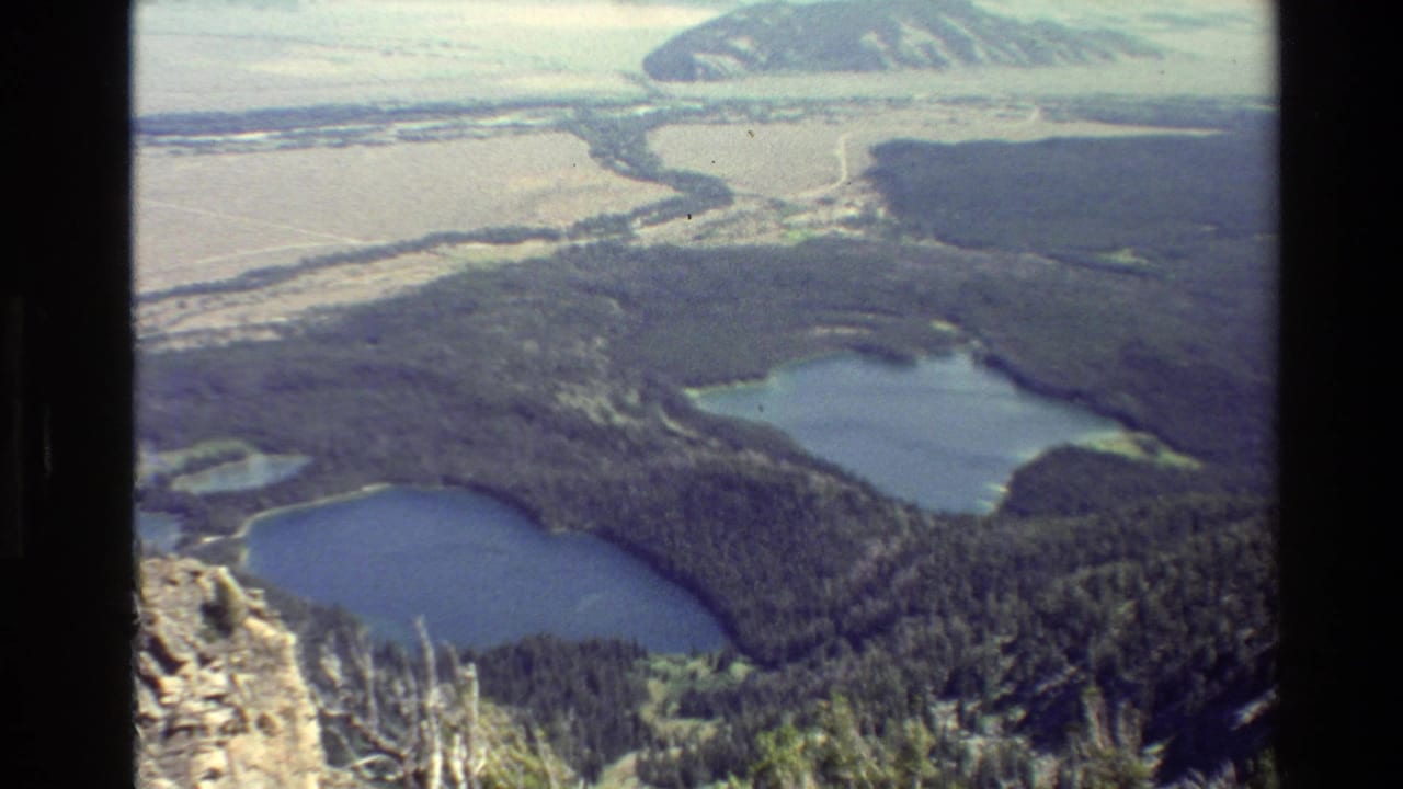 Mountain valley view with forest, paired lakes, distant ridge, and dark vertical frame edge.