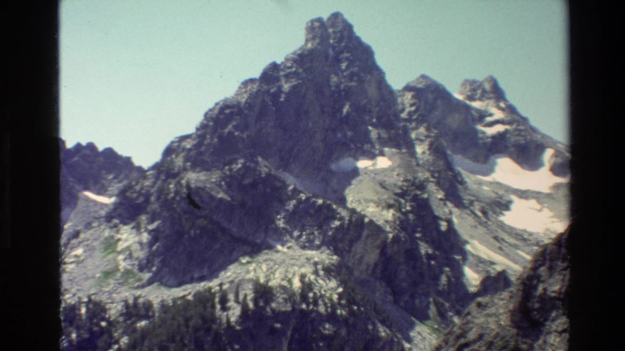 Jagged rocky mountain peaks with small snow patches under a pale sky.