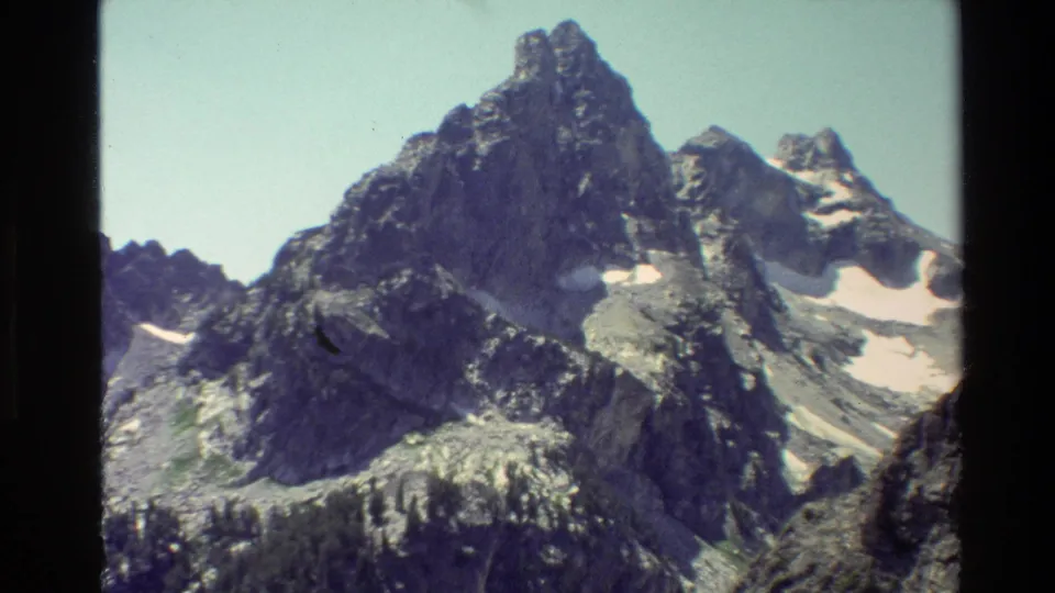 1980 8mm view of Grand Teton rocky peaks with scattered snow patches and dark film borders.
