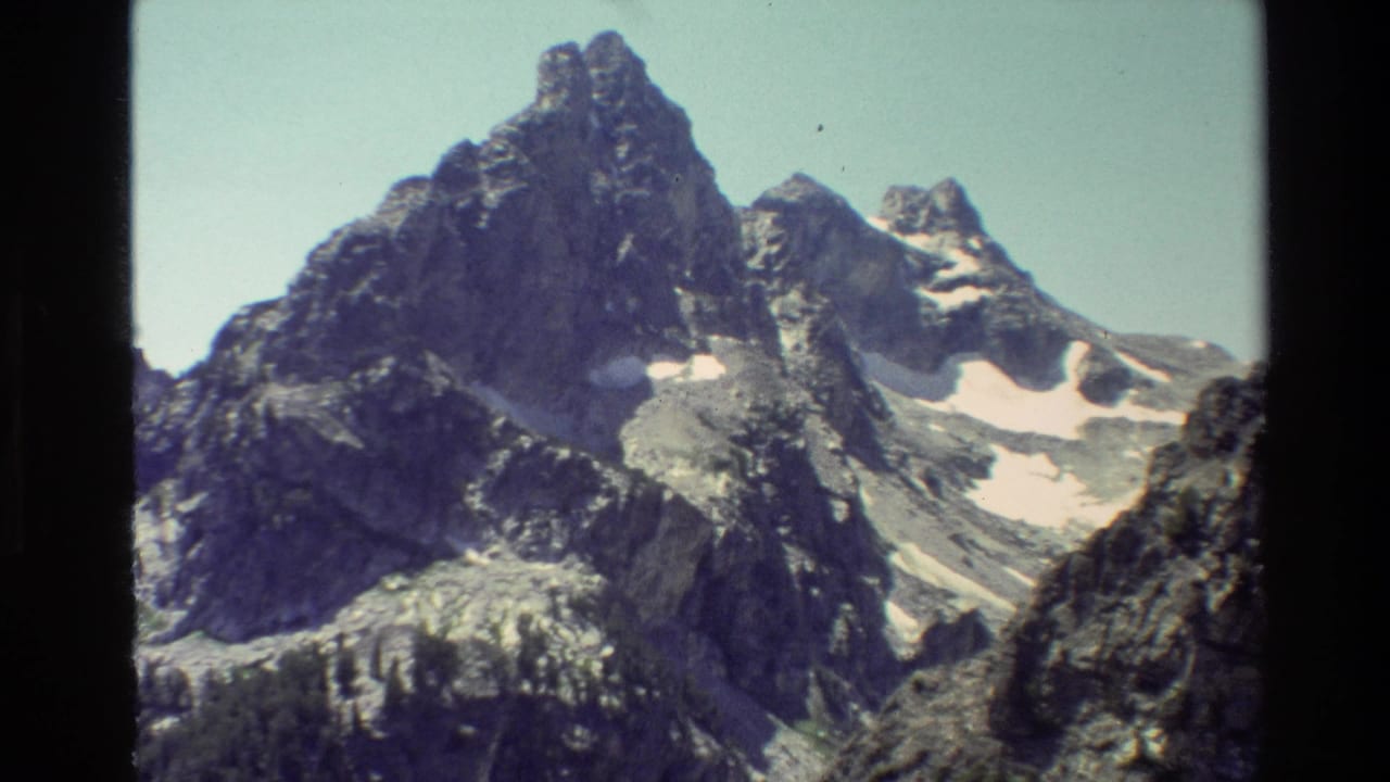 Grand Teton mountain view on 8mm film, showing a tall rocky peak and lingering snow beneath a clear sky.