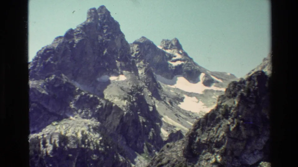 1980 8mm Grand Teton view with rugged peaks, pale snowfields, and a dark rocky slope at the right edge.