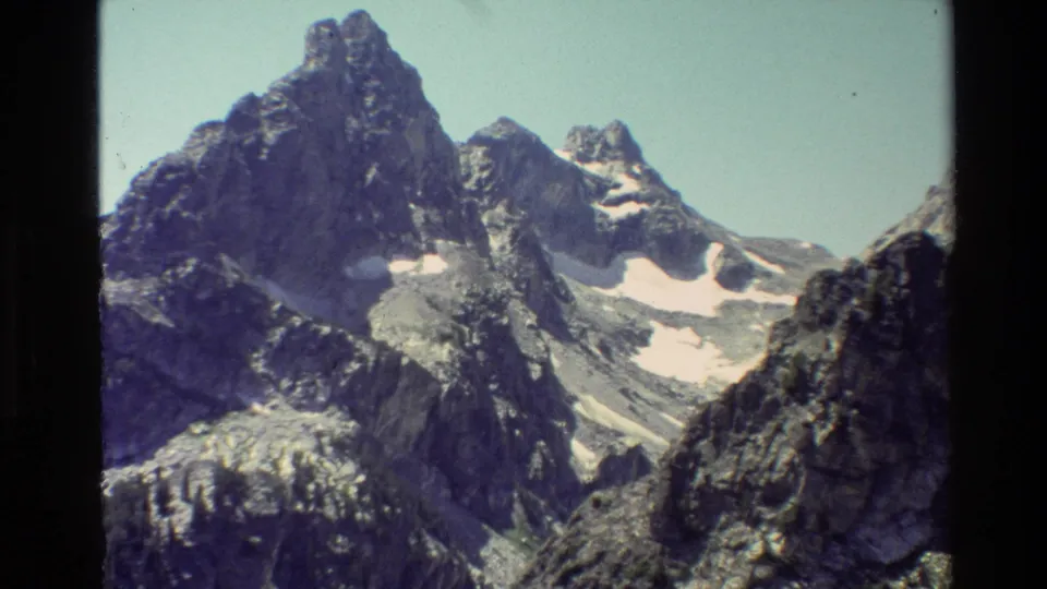 Grand Teton peaks in 1980 home-movie footage, with snow patches, shaded rock, and visible 8mm frame borders.
