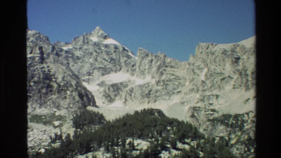 Grand Teton, Wyoming landscape frame with rugged stone ridges, white snowfields, and dark conifers below.