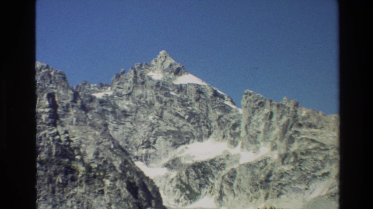 Similar mountain view with snow patches, blue sky, and dark vertical film border.
