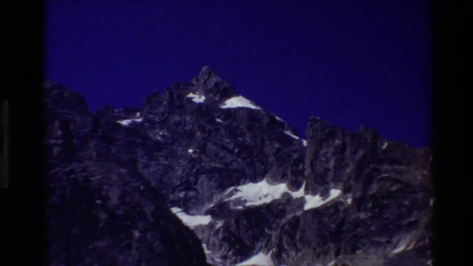 Blue-shifted 1980 8mm frame of the Grand Teton range, with snow patches standing out against dark rock.