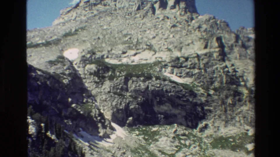 Final 1980 8mm frame of Grand Teton with rugged rock layers, small snowfields, blue sky, and visible contact-sheet framing.