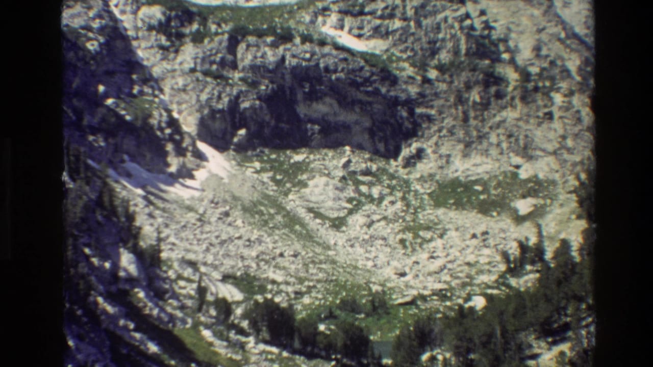 Grand Teton, Wyoming frame from 1980 showing a cliff-like mountainside, talus, snow remnants, and conifer growth.