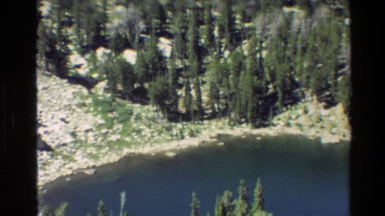 Evergreen trees surround a dark alpine lake with rocky shoreline visible above the water.