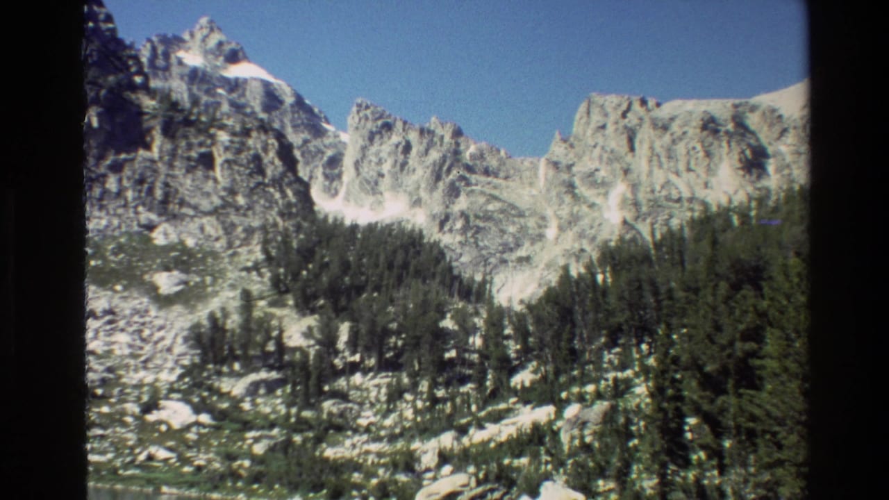 Snow-streaked mountain peaks above dense pine forest with black 8mm frame borders.