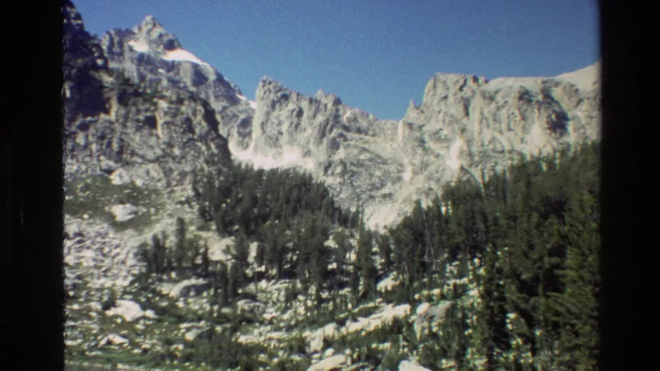 Grand Teton, Wyoming mountain landscape with pale rock faces, snow patches, and conifer forest in vintage 8mm footage.