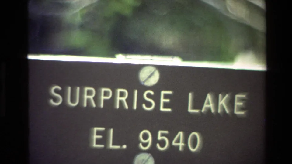 Close 1980 8mm frame of a Surprise Lake elevation sign reading EL. 9540, with soft green foliage in the background.