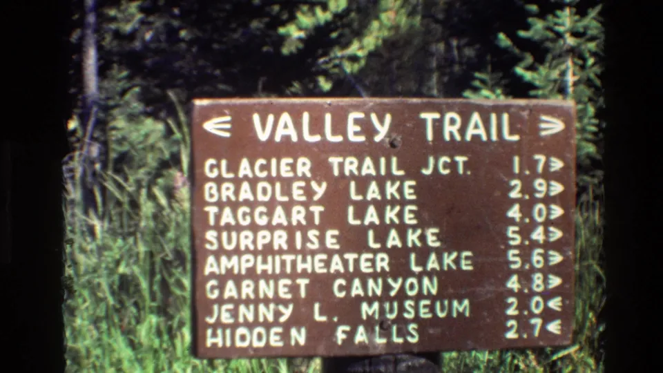 1980 Grand Teton 8mm frame showing the Valley Trail sign with entries for Surprise Lake, Amphitheater Lake, Garnet Canyon, Jenny L. Museum, and Hidden Falls.