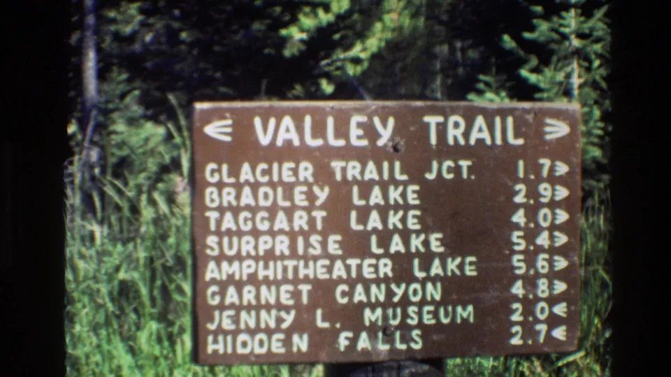 Final frame of the Grand Teton Valley Trail sign, with destination names and distance arrows visible through soft 8mm film grain.