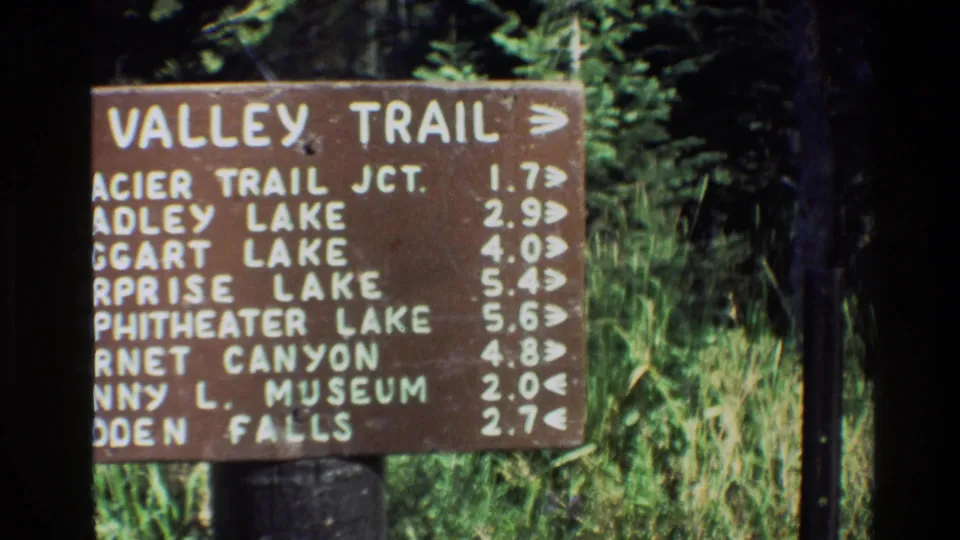 End frame crops the left side of the Grand Teton Valley Trail sign while keeping the white mileage listings and surrounding grasses visible.