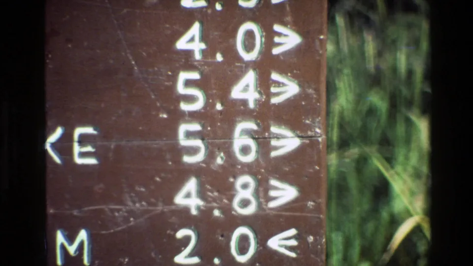 Final close-up frame of the Grand Teton Valley Trail sign, showing worn brown wood, white arrows, and distance markings.