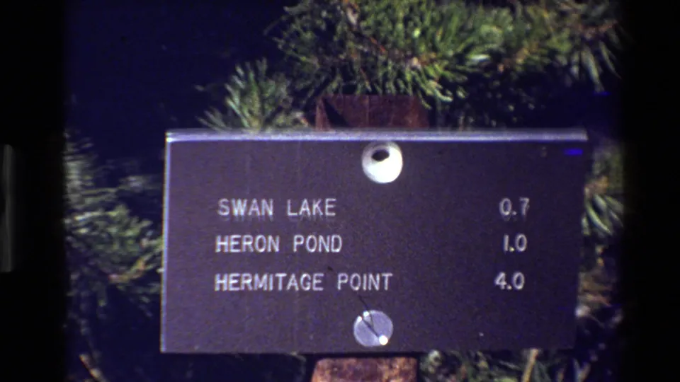 Grand Teton park direction sign listing Swan Lake, Heron Pond, and Hermitage Point, filmed close-up on 8mm in 1980.