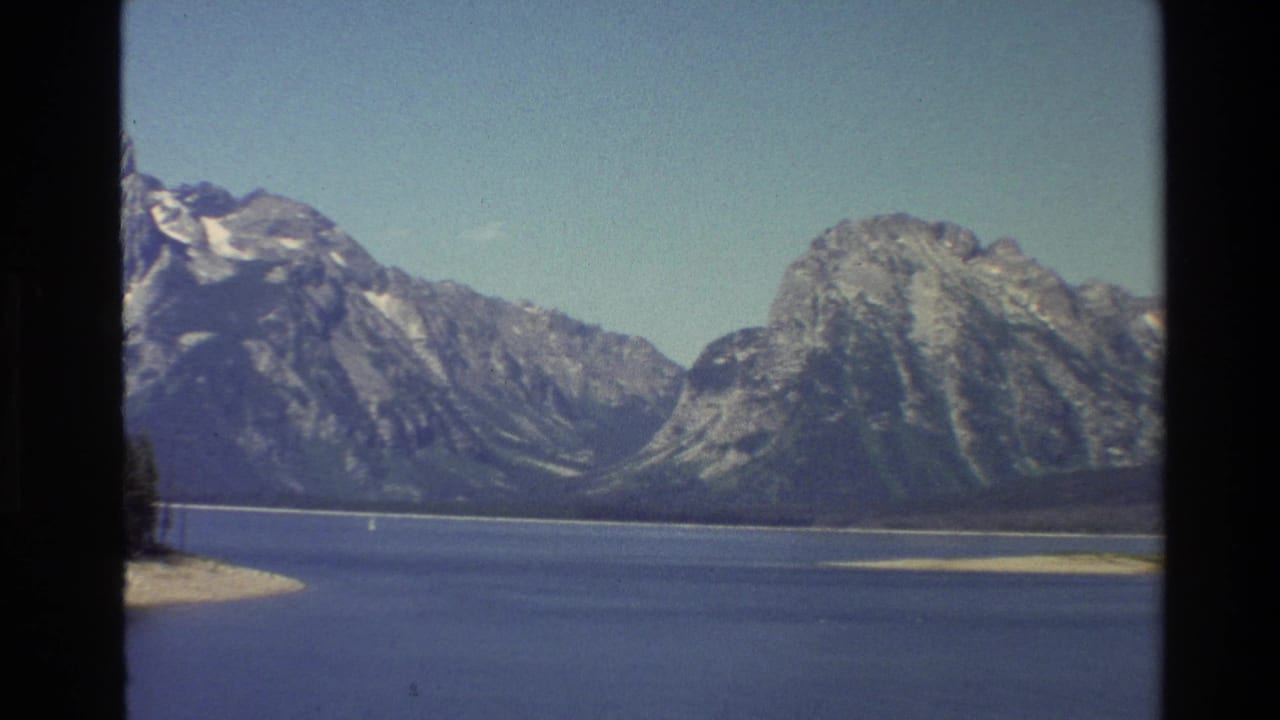 Mountain peaks and a broad lake seen through dark vertical borders under a clear blue sky.