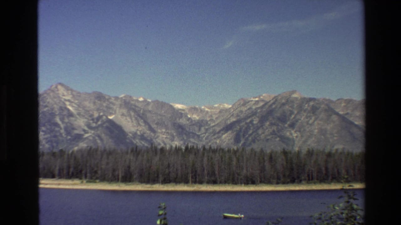 Small motorboat on a lake before forest and mountains.
