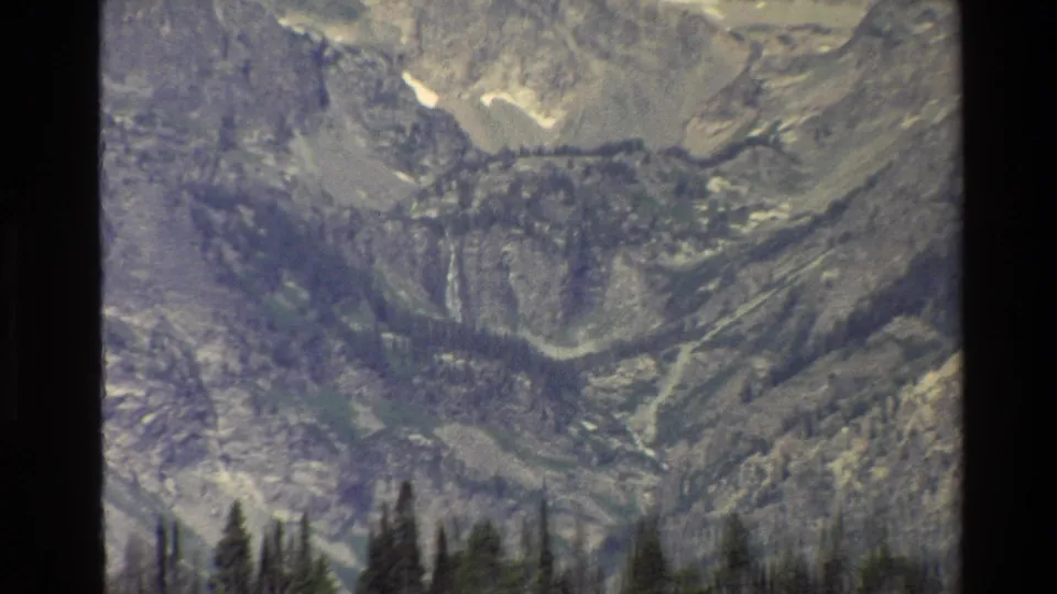 Zoomed 1980 Grand Teton mountain view with gray rock walls, patches of snow, and evergreens along the lower edge.