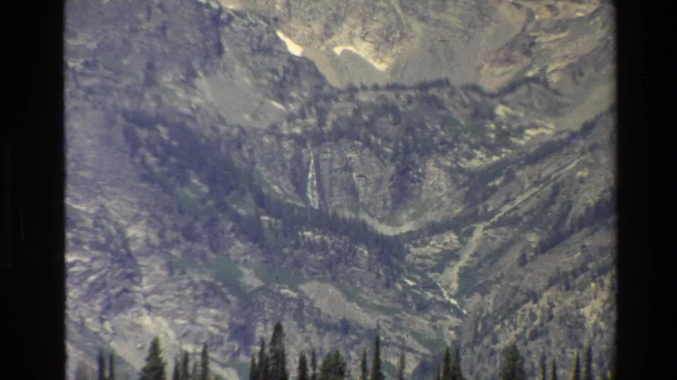 Closer 8mm view of Grand Teton terrain, with forest silhouettes below pale rocky slopes and small remaining snow patches.